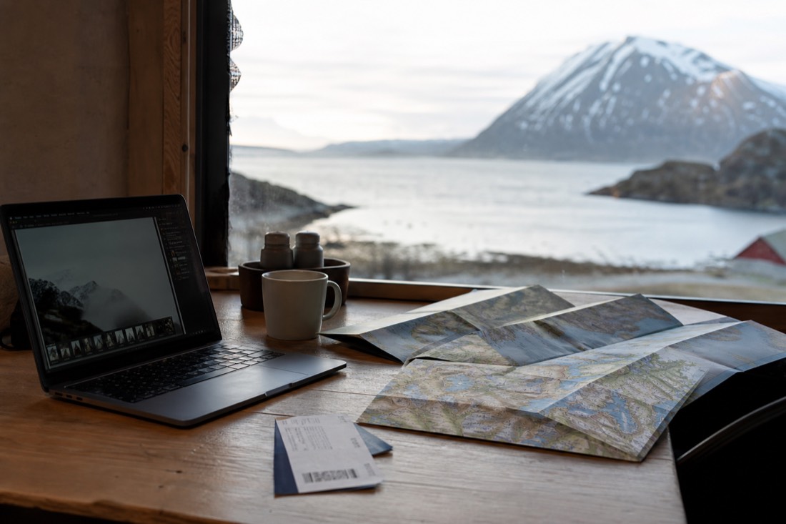 Desk with an open laptop, a printed boarding pass and a Norway map folded to the west coast