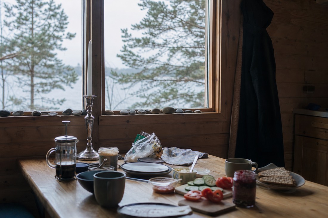 Family cabin kitchen table with breakfast things and a window onto pine trees and water