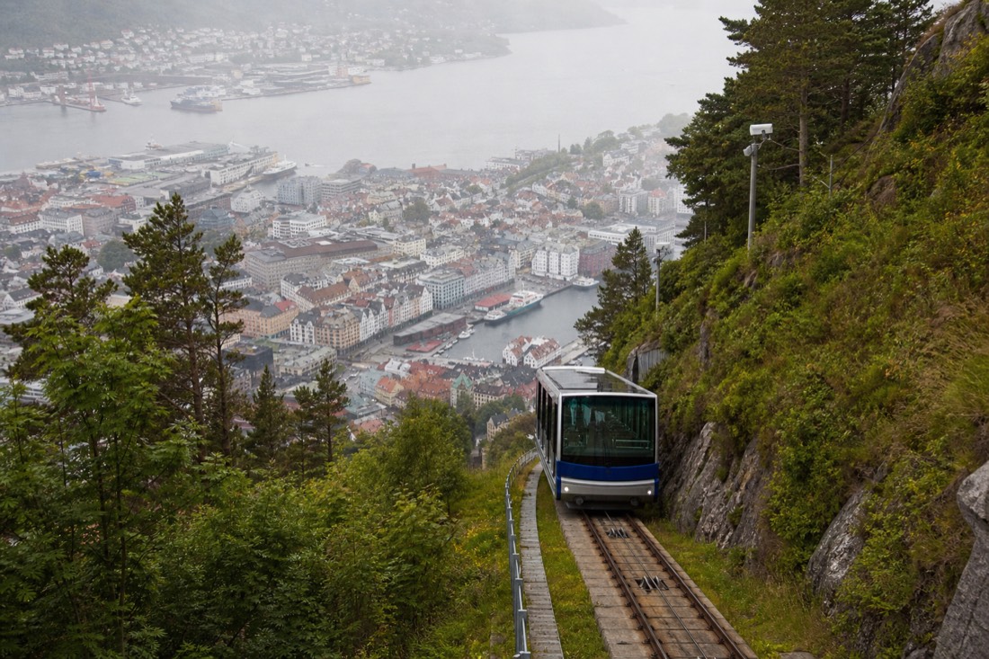 Small funicular carriage climbing a green hillside above a harbour city