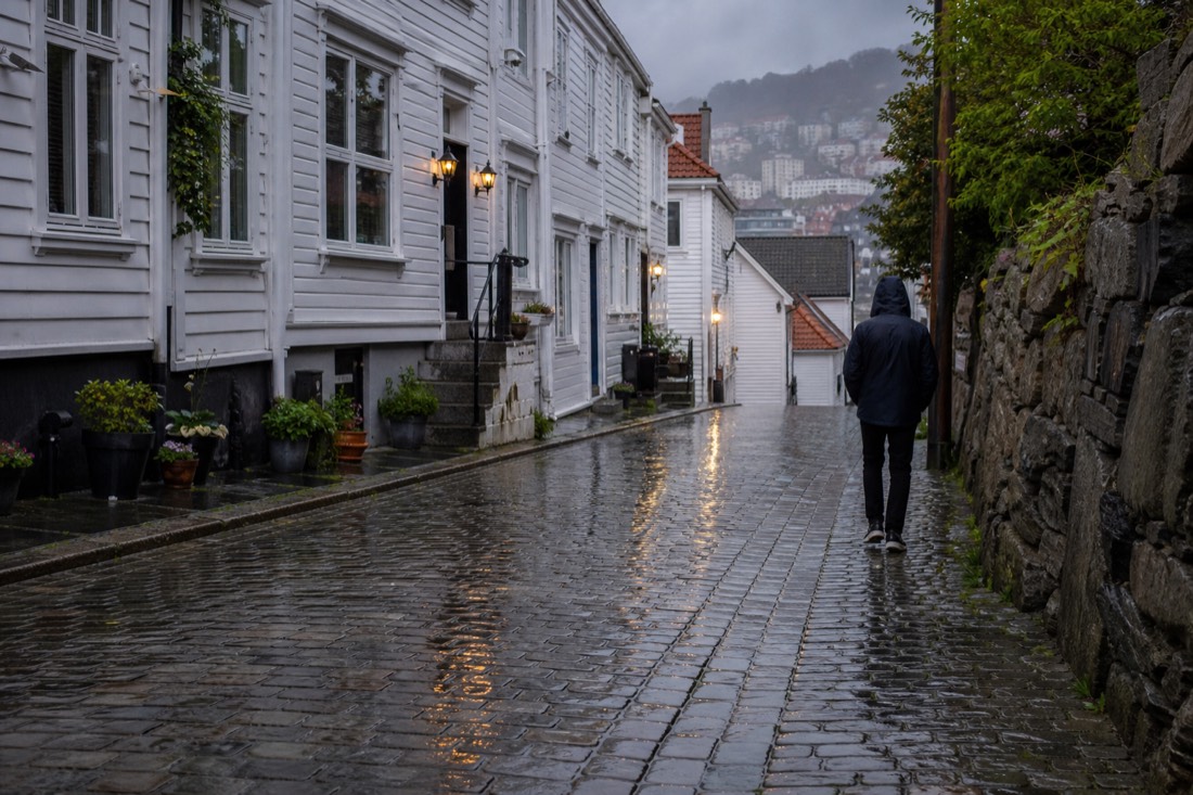 Wet cobbled street in Bergen with an umbrella-less pedestrian in a rain shell and reflections underfoot