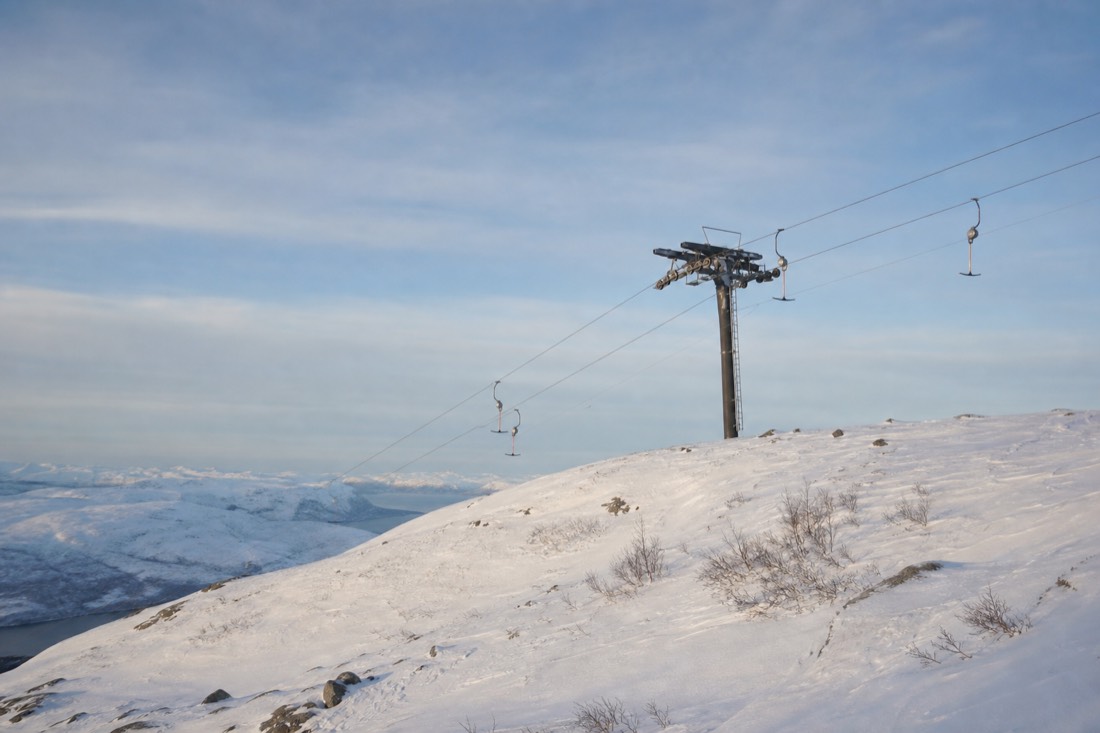Ski lift pylon on a rounded snowy Norwegian hillside under a pale blue winter sky