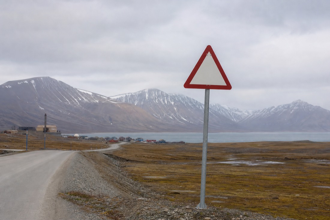 Warning sign post at the edge of an Arctic settlement road with tundra and mountains beyond