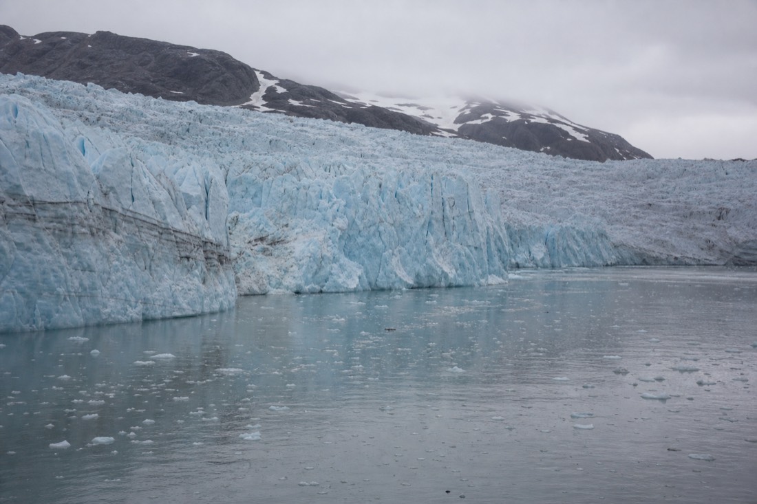 Glacier front meeting dark Arctic water with drifting ice under flat grey light