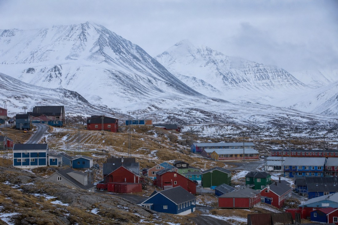 Colourful wooden buildings of an Arctic settlement with snow-covered mountains behind