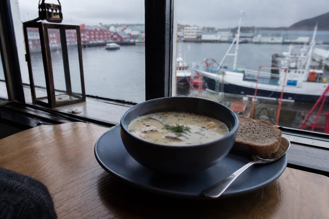 Bowl of creamy fish soup with bread on a wooden table by a harbour window