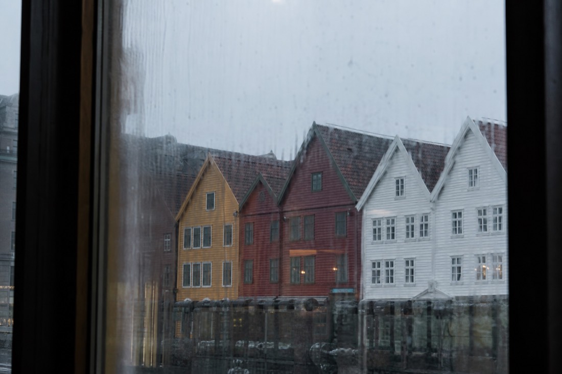 View through a rain-streaked cafe window onto the coloured wooden fronts of Bryggen