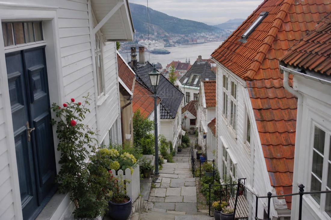 Steep narrow lane of white wooden houses climbing a hillside above Bergen with flower pots on steps