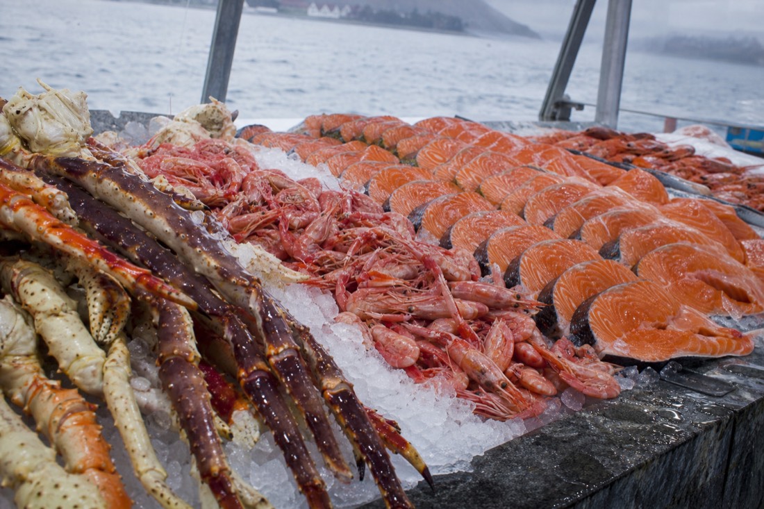 Crushed ice counter of a Norwegian fish market piled with king crab legs, shrimp and salmon fillets