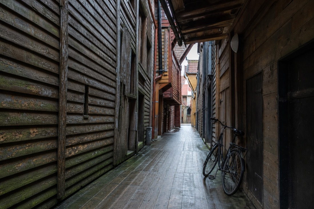 Narrow wooden alley behind the Bryggen warehouses with worn plank walls and a bicycle