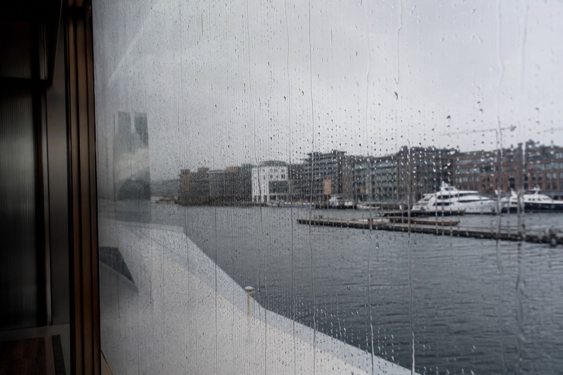 Rain running down a large museum window in Oslo with the blurred harbour beyond