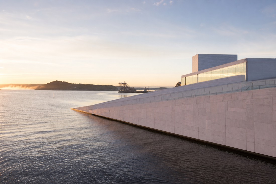 The sloping white marble roof of the Oslo Opera House with the fjord and morning light beyond