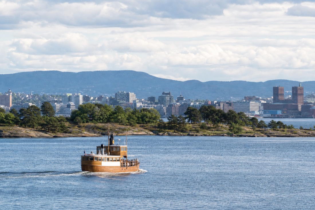 Small wooden ferry crossing the Oslofjord past low green islands with the city skyline behind
