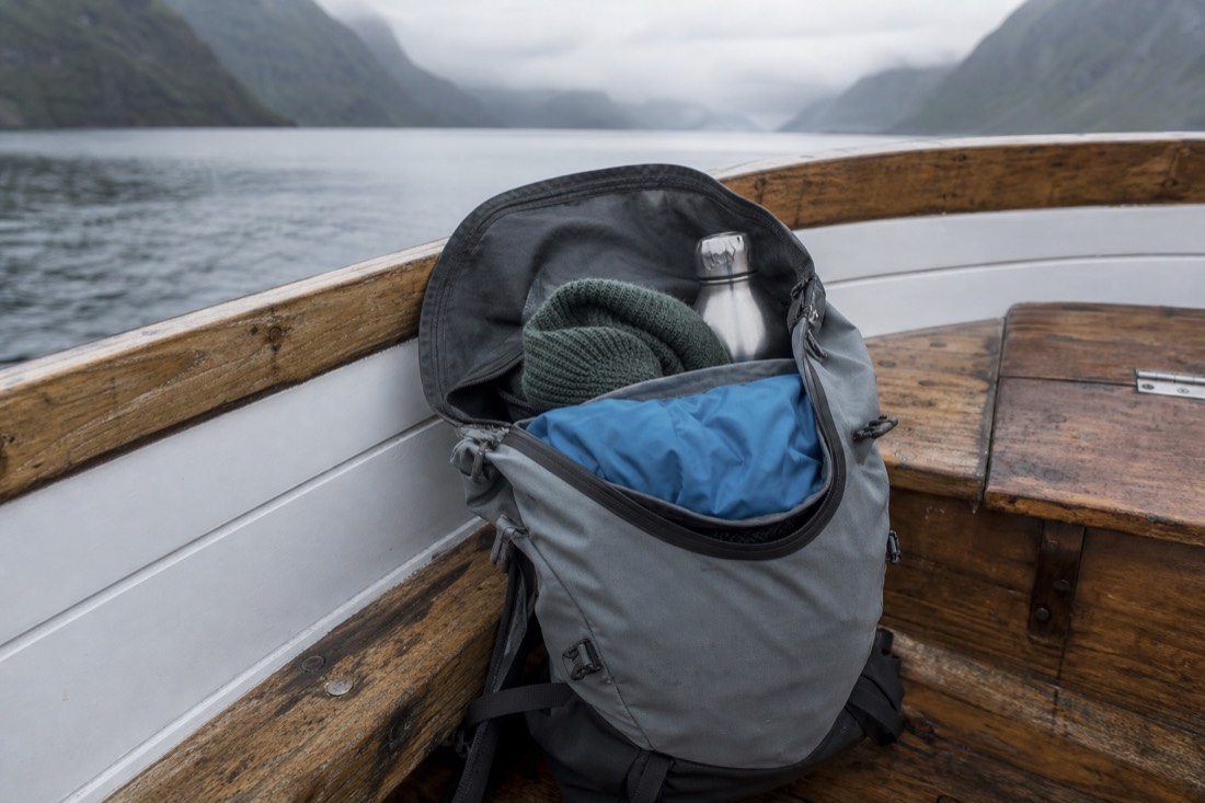 Open day pack on a boat bench with a folded rain shell, wool hat and water bottle inside