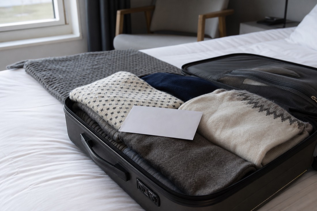 Open suitcase on a bed with folded wool layers, a customs declaration card resting on top