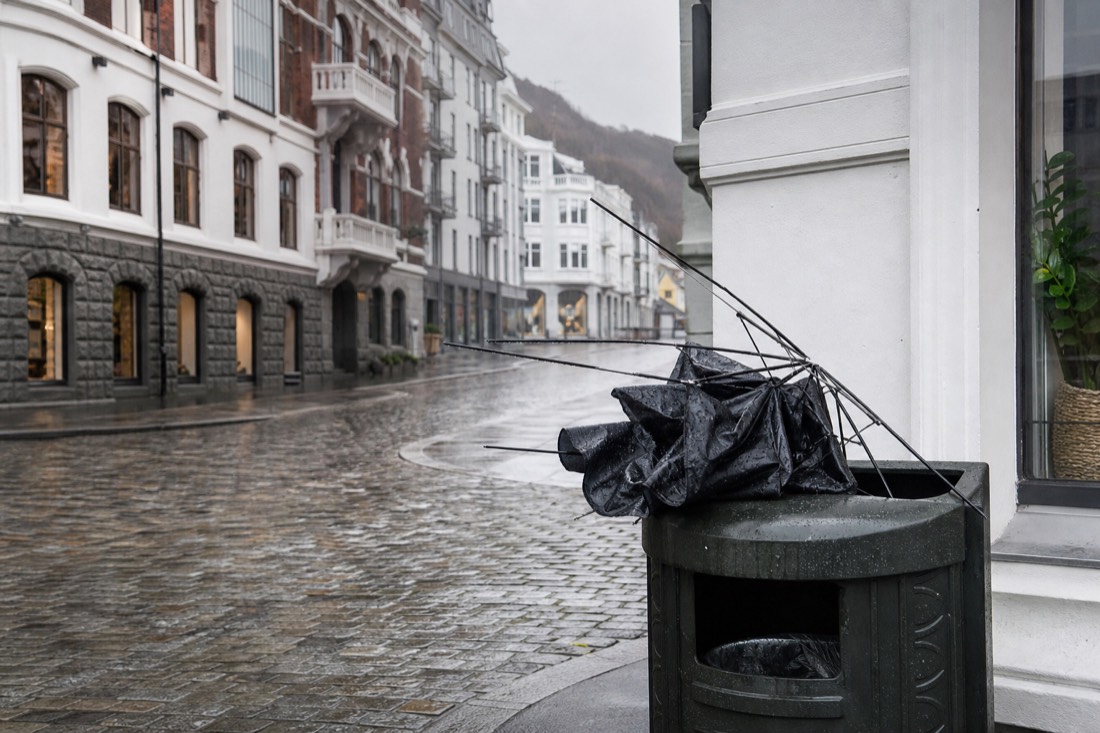 A broken umbrella in a public bin on a windy Bergen street with wet cobblestones