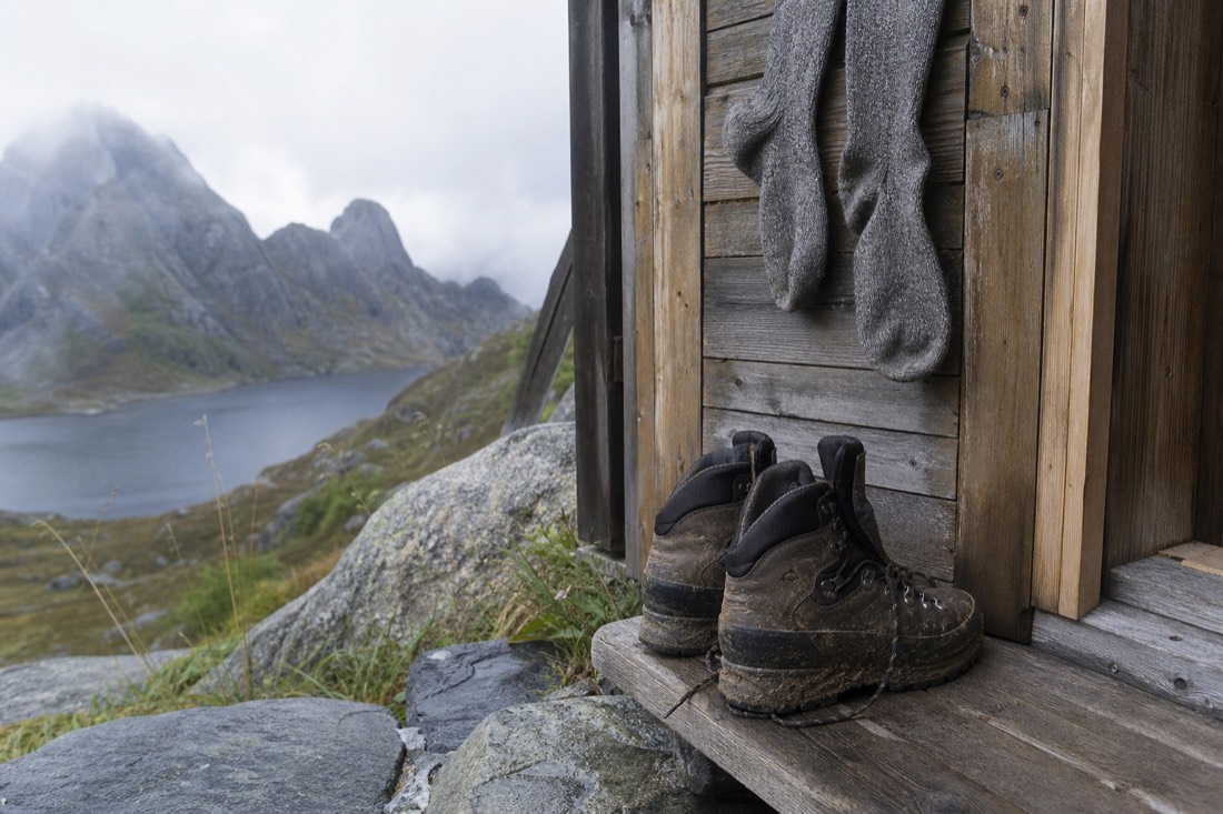 Well-worn waterproof hiking boots and wool socks drying beside a wooden cabin doorway